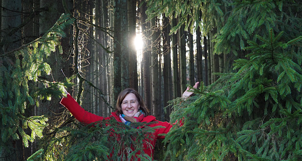 Anita Griebl im Wald zwischen Tannen im Sonnenlicht – Symbol für Heilung, Lebensfreude und den Weg aus der Depression.