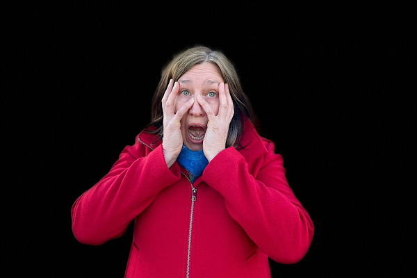 Symbolbild für Angst: Anita Griebl mit erschrockenem Gesicht und großen Augen vor dunklem Hintergrund – Angst überwinden.