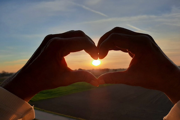 Zwei Hände formen ein Herz, durch das die Sonne scheint – ein Symbol für Dankbarkeit und innere Verbundenheit.