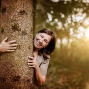 Anita Griebl blickt hinter einem Baum hervor – ein Moment der Verbundenheit mit der Natur und dem inneren Wandel.