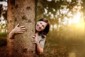 Anita Griebl blickt hinter einem Baum hervor – ein Moment der Verbundenheit mit der Natur und dem inneren Wandel.
