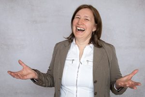 Anita Griebl lacht voller Freude in die Kamera, die Hände offen zum Empfang – Symbolbild für Befreiung, Selbstannahme und das Loslassen alter Glaubenssätze.
