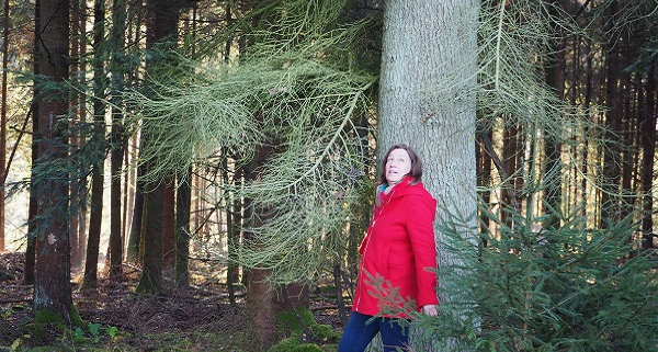 Rotjäckchen im Wald: Frau mit rotem Jäckchen steht angelehnt an einem Baum und schaut in die Ferne.