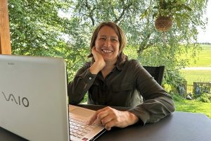 Der-lange-Weg-zum-Erfolg-SchreibWG Anita sitzt mit ihrem Laptop im Garten und arbeitet konzentriert, umgeben von natürlichem Grün.