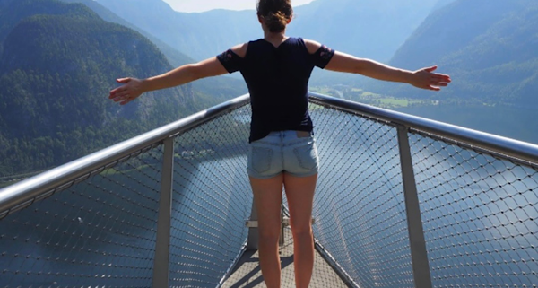 Junge Frau steht mit ausgebreiteten Armen auf einem Steg am Wasser und symbolisiert Freiheit und innere Leichtigkeit.