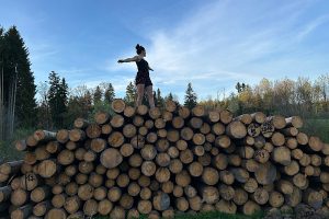 Tabitha balanciert auf Baumstämmen im Wald – Symbol für innere Stärke und den Weg aus der Trauer.