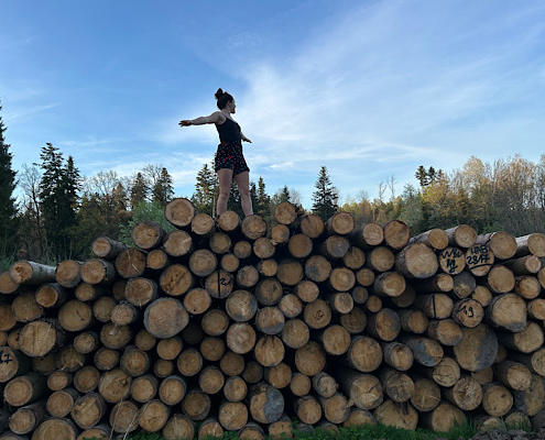Tabitha balanciert auf Baumstämmen im Wald – Symbol für innere Stärke und den Weg aus der Trauer.