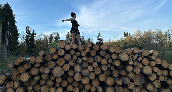 Tabitha balanciert auf Baumstämmen im Wald – Symbol für innere Stärke und den Weg aus der Trauer.