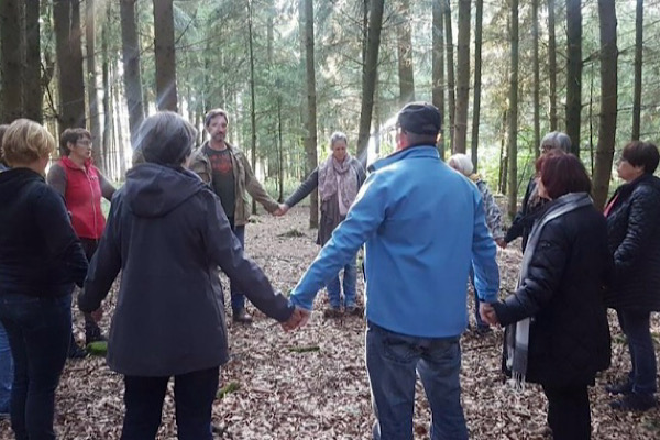 Menschen stehen im Seminar im Kreis. Sie fühlen die Verbundenheit in der Natur bei einer Meditation.