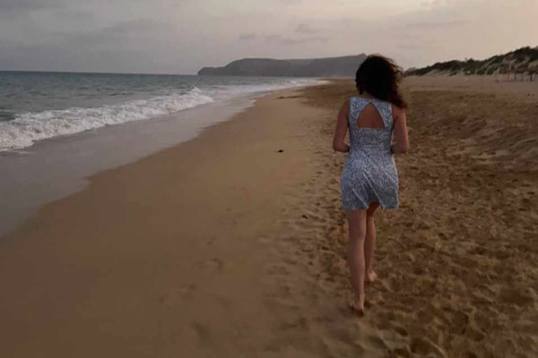 Eine junge Frau geht im Sand am Meer entlang - Ein Zeichen, um mehr zu fühlen.