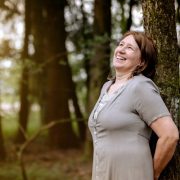 Anita Griebl im Wald, an einen Baum gelehnt, mit weitem Blick – Moment der Einkehr, Energiearbeit und intuitiven Selbstverbindung