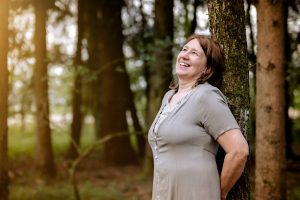 Anita Griebl im Wald, an einen Baum gelehnt, mit weitem Blick – Moment der Einkehr, Energiearbeit und intuitiven Selbstverbindung