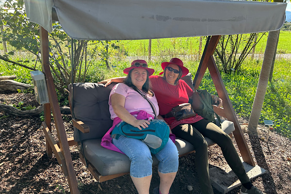 „Heidi und Anita genießen eine Pause in der Hollywoodschaukel – eingebettet in Blüten, Begegnung und sommerlicher Leichtigkeit.