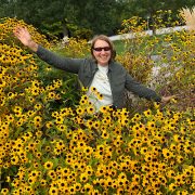 Anita Griebl mit Sonnenbrille sitzt zwischen gelben Blüten – ein Moment der stillen Freude und inneren Fülle.