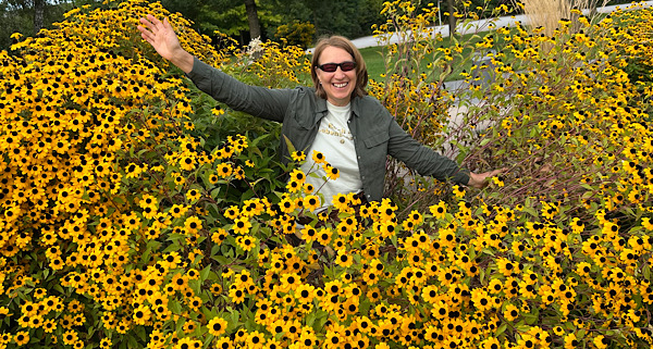 Anita Griebl mit Sonnenbrille sitzt zwischen gelben Blüten – ein Moment der stillen Freude und inneren Fülle.