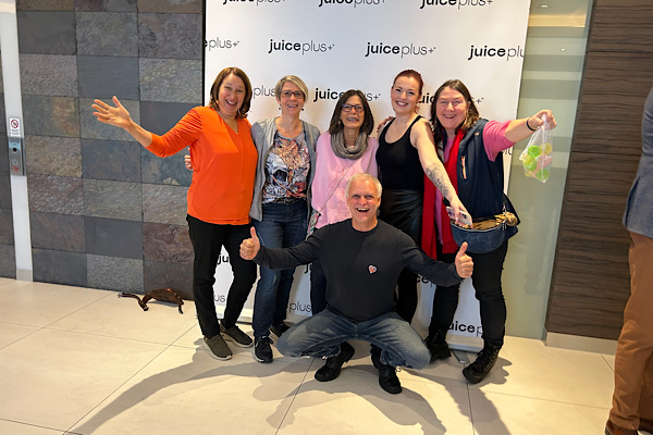 Gruppenfoto vor dem Juice+ Plakat – sechs Partner:innen präsentieren sich mit strahlender Energie und gemeinsamer Ausrichtung.