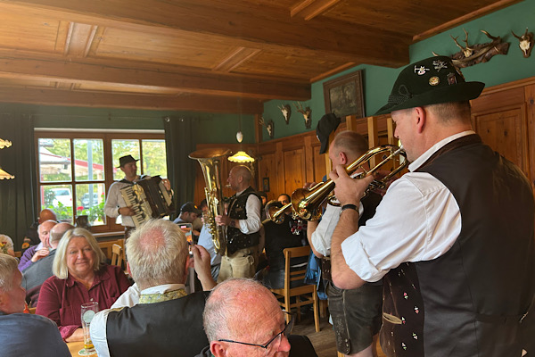 Kirchweihstimmung im Gasthaus Lindner Bräu – Menschen im Gespräch und vier Musiker der Blaskapelle sorgen für festliche Atmosphäre.