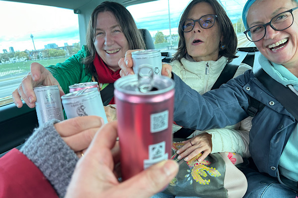 Frauen stoßen im Ubertaxi mit Proseccodosen an – ein Moment voller Freude und gemeinsamer Reise.