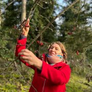 Anita Griebl in roter Jacke hält einen Zweig mit Hagebutten im Wald fest.