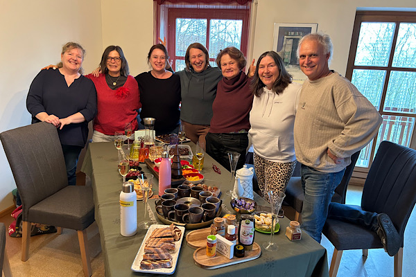 Sieben Teampartner:innen beim Advents-Team-Treffen, lachend und verbunden, gemeinsames Feiern und Austausch in herzlicher Atmosphäre.