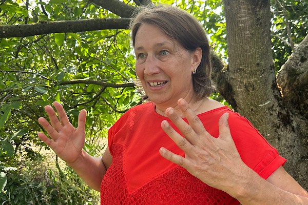 Anita Griebl steht seitlich in der Natur und hebt beide Hände in einer offenen, energetischen Geste.