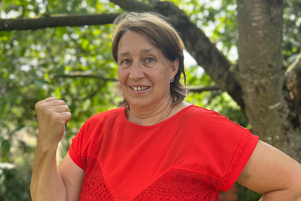 Anita Griebl schaut freundlich in die Kamera und hebt in der Natur eine Faust als Zeichen von Stärke.