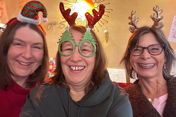 Drei Frauen – Heidi, Claudia und Anita – lachen in die Kamera und tragen weihnachtlichen Kopfschmuck.