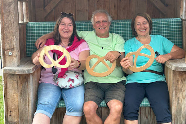 Anita Griebl, Heidi und Franz sitzen in einem Strandkorb auf dem Donaufest in Deggendorf und halten Holzbrezen in den Händen.