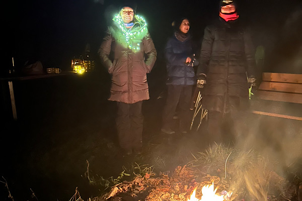 Eine Frau steht vor einem brennenden Feuer und trägt eine Lichterkette um den Hals.