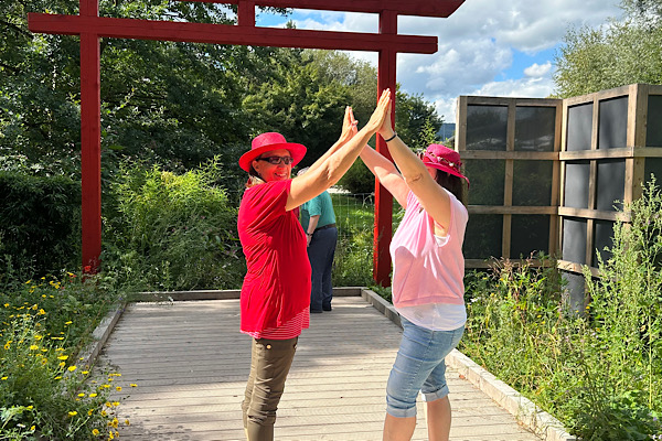 Anita Griebl und Heidi stehen sich in der Gartenschau in Furth im Wald gegenüber und halten sich an den Händen, sodass eine Brücke entsteht.