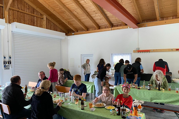 Anita Griebl und ihre Nachbarn bei einem Straßenfest in ihrer Halle; wegen des schlechten Wetters findet das Fest drinnen statt.