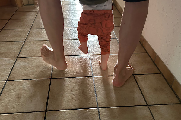 Nackte Füße von Großvater und eineinhalbjährigem Enkel, von hinten aufgenommen – die kleinen Füßchen in der Mitte als berührender Familienmoment.