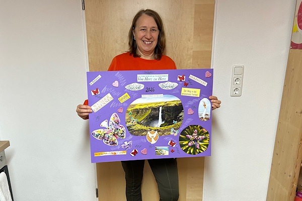 Anita steht mit ihrem gestalteten Visionsplakat im Raum und hält es gut sichtbar vor sich.