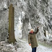 Anita Griebl steht im winterlichen Wald und zieht an einem Fichtenzweig, sodass Schnee auf sie herabfällt.