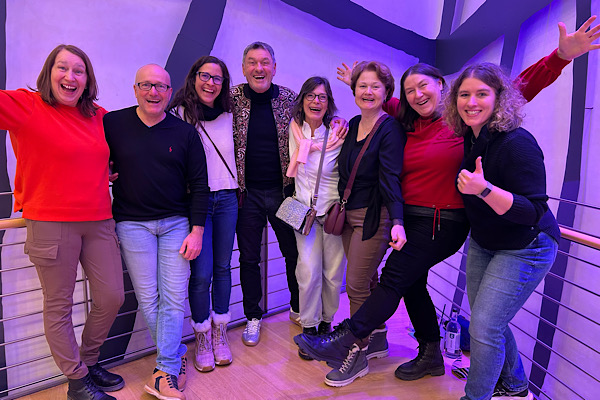 Teammitglieder strecken lachend die Hände nach vorne und posieren gemeinsam.