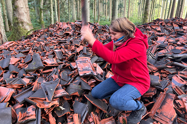 Anita zerhaut auf dem Wutberg einen Dachziegel, umgeben von Wald.