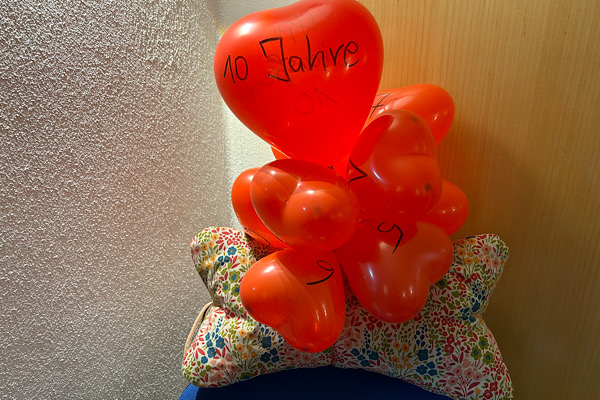 Ein Geschenk mit roten Luftballons, von denen einer die Aufschrift ‚10 Jahre Treffpunkt Lebensfreude‘ trägt.