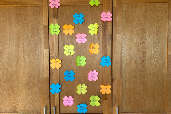 Ein Schrank mit 21 bunten Papier‑Kleeblättern, auf denen persönliche Sätze zur 21‑Tage‑Challenge ‚Lebensenergie und Lebensfreude‘ notiert sind.