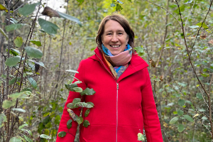 Anita Griebl geht lächelnd durch den Wald und blickt in die Kamera.