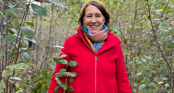 Anita Griebl geht lächelnd durch den Wald und blickt in die Kamera.