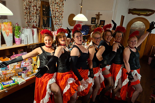 Sieben Frauen im Can‑Can‑Kostüm beim Frauenfasching beim Heinerl, seitlich nebeneinander stehend und ihre roten Strumpfbänder zeigend.