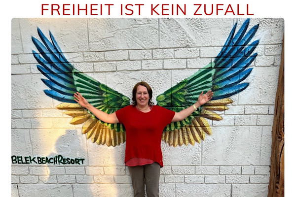 Anita Griebl steht vor einem Kunstwerk mit ausgebreiteten Flügeln – Symbol für innere Freiheit im Seminar, Freiheit ist kein Zufall.