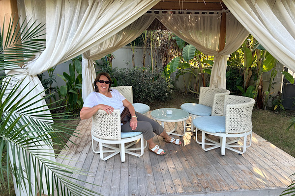 Anita sitzt unter einer mit Stoff behangenen Sitzgruppe; ein leiser Moment von Nähe zu sich selbst, Ruhe und alltäglicher Lebensfreude.