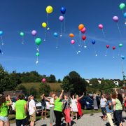 Menschen lassen bunte Luftballons in den Himmel steigen – ein Symbol für Leichtigkeit, Gemeinschaft und Lebensfreude.