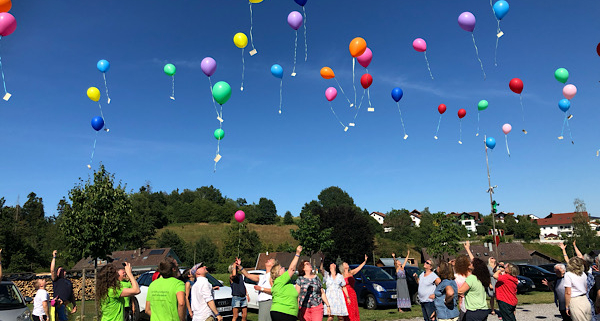 Menschen lassen bunte Luftballons in den Himmel steigen – ein Symbol für Leichtigkeit, Gemeinschaft und Lebensfreude.