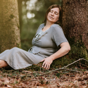 Anita Griebl sitzt mit geschlossenen Augen vor einem Baum im Wald und verbindet sich mit ihren Gefühlen und Emotionen.
