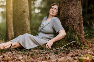 Unterschied zwischen Gefühle und Emotionen Anita Griebl sitzt mit geschlossenen Augen vor einem Baum im Wald und verbindet sich mit ihren Gefühlen und Emotionen.