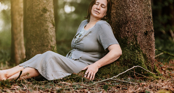 Anita Griebl sitzt mit geschlossenen Augen vor einem Baum im Wald und verbindet sich mit ihren Gefühlen und Emotionen.