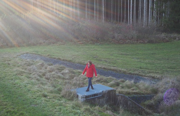 Anita Griebl steht auf einem Wasserreservoir in einer herbstlichen Waldwiese, umgeben von Sonnenlicht – Symbol für Persönlichkeitsstärkung und innere Klarheit.