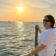 Anita steht am Meer im warmen Abendlicht und schaut seitlich zurück; ein ruhiger Moment von Verbundenheit und innerer Klarheit.